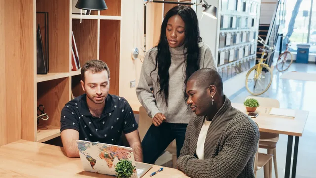 A diverse team discussing ideas around a laptop in a contemporary office setting. Community onboarding and member activation